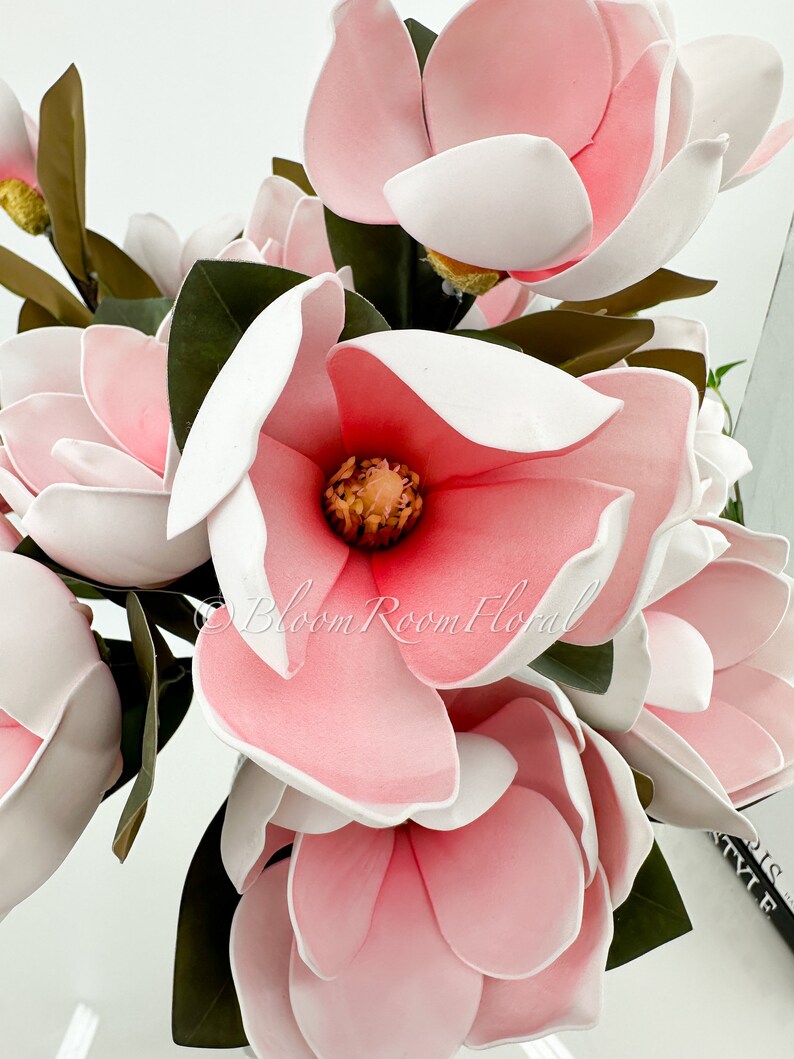 May include: A bouquet of pink and white magnolia flowers with green leaves. The flowers have a white center and pink petals.