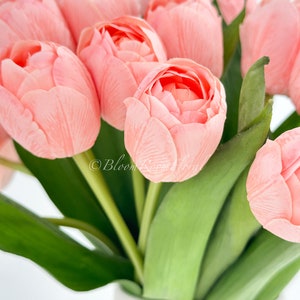 May include: A bouquet of pink tulips with green stems in a white vase. The tulips are arranged in a cluster, with the stems extending out from the center. The vase is simple and elegant, with a smooth white finish.