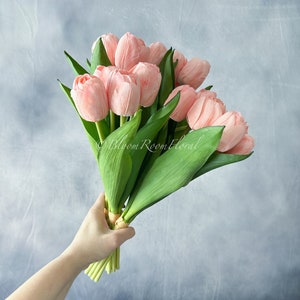 May include: A bouquet of pink tulips with green stems and leaves. The tulips are arranged in a hand-tied bouquet.