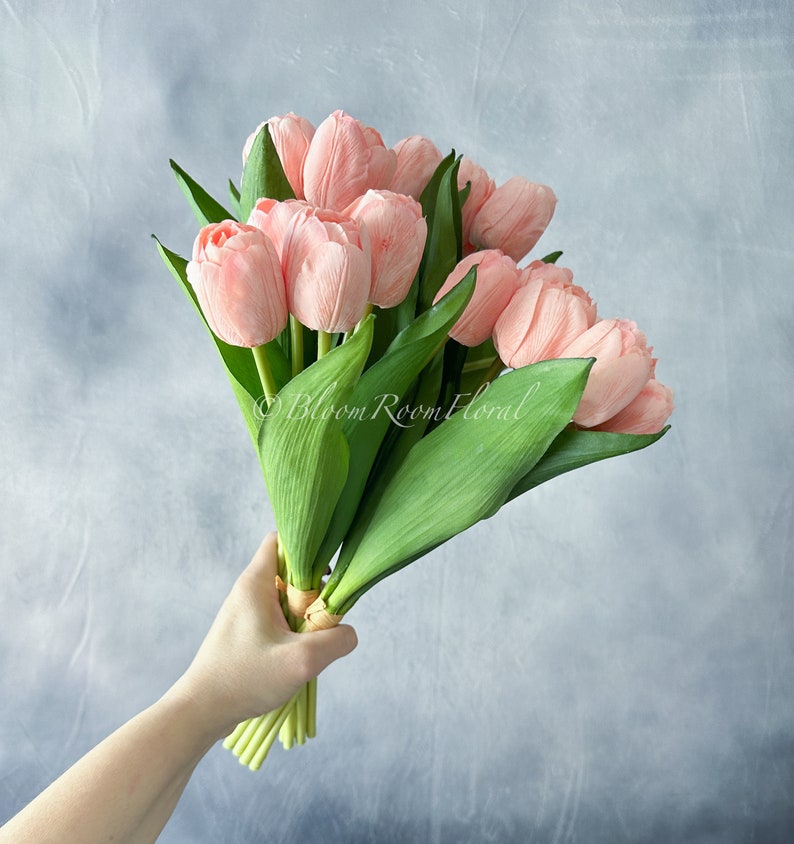 May include: A bouquet of pink tulips with green stems and leaves. The tulips are arranged in a hand-tied bouquet.