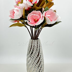 May include: A bouquet of pink and white magnolia flowers in a silver vase with a textured design.