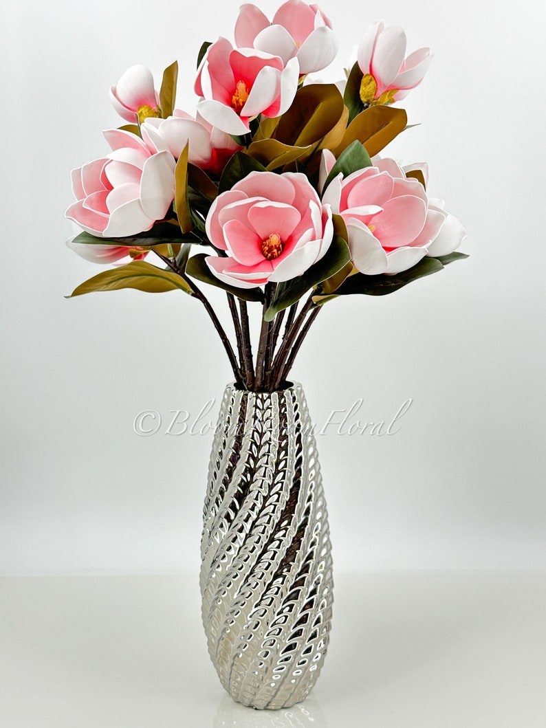 May include: A bouquet of pink and white magnolia flowers in a silver vase with a textured design.