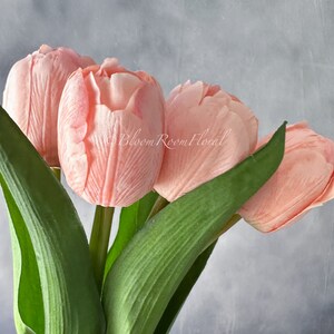 May include: A bouquet of four pink artificial tulips with green stems and leaves.