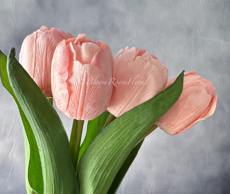 May include: A bouquet of four pink artificial tulips with green stems and leaves.