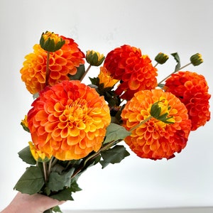 May include: A bouquet of orange and yellow dahlia flowers with green leaves.