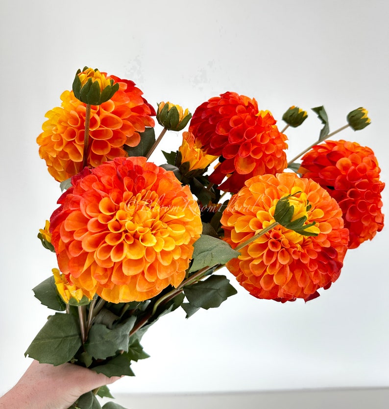 May include: A bouquet of orange and yellow dahlia flowers with green leaves.