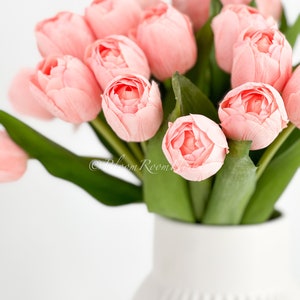 May include: A bouquet of pink tulips arranged in a white ceramic vase with a ribbed design.