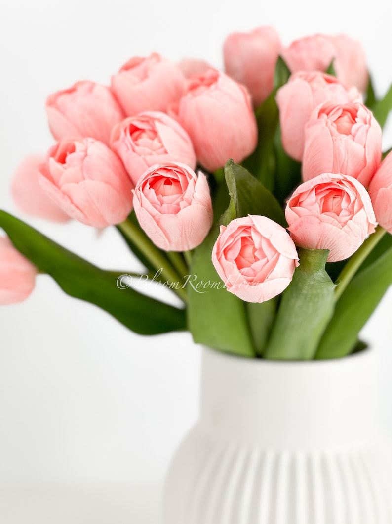 May include: A bouquet of pink tulips arranged in a white ceramic vase with a ribbed design.