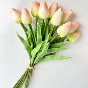 May include: A bouquet of 10 faux pink and white tulips with green stems and leaves. The stems are tied together with a beige ribbon.