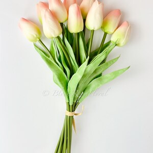 May include: A bouquet of 10 pink and white artificial tulips with green stems and leaves. The stems are tied together with a brown ribbon.