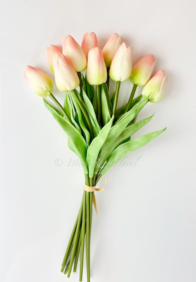 May include: A bouquet of 10 pink and white artificial tulips with green stems and leaves. The stems are tied together with a brown ribbon.
