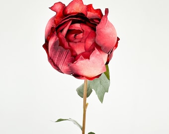 May include: A single, artificial rose with a large, fully bloomed head in shades of deep red and pink. The petals have a textured appearance. The stem is a light brown color with green leaves. The flower is set against a plain white background.