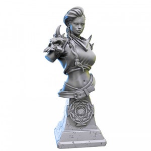 Puede incluir: Un busto de escultura gris de una mujer con un peinado trenzado, que lleva un cinturón de cuero y una pieza de hombro decorativa con un diseño de calavera. El busto está sobre un pedestal gris con un diseño geométrico.