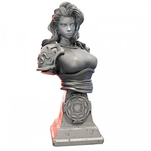 Puede incluir: Un busto de escultura gris de una mujer con el pelo largo, que lleva una parte superior decorativa y una faja. El busto está montado sobre una base de piedra con un diseño circular.