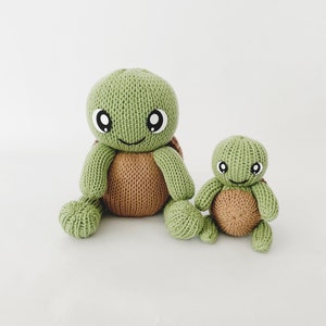 Könnte beinhalten: Zwei gestrickte grüne und braune Schildkrötenspielzeuge. Die größere Schildkröte hat ein lächelndes Gesicht mit schwarzen Augen. Die kleinere Schildkröte sitzt neben der größeren.