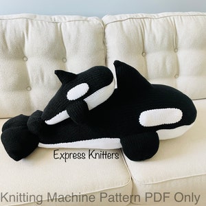 Peut inclure: Deux peluches orques tricotées en noir et blanc sur un canapé blanc. La plus grande orque est couchée sur le côté, la tête reposant sur la plus petite orque. Le texte "Express Knitters" est visible sous les orques.