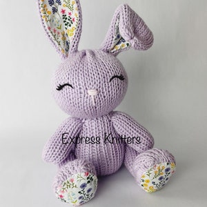 May include: A lavender knitted bunny with floral fabric accents on the ears and feet. The bunny has a sweet expression with embroidered eyes and a pink nose.