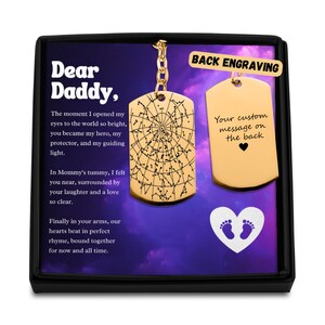 May include: Gold-colored dog tag pendant with a constellation design and the words "Dear Daddy." The pendant is displayed in a black box with a purple background. The back of the pendant is blank and can be engraved.