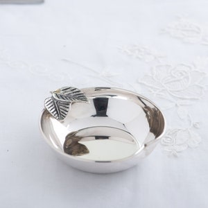 Może przedstawiać: Srebrna miska z wzorem liścia po bokach. Miska jest błyszcząca i odbija światło.