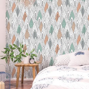 May include: A wall covered in a repeating pattern of stylized trees in shades of white, black, gray, teal, and peach. A small wooden table holds a plant and a black alarm clock. A bed with a patterned comforter is in the foreground.