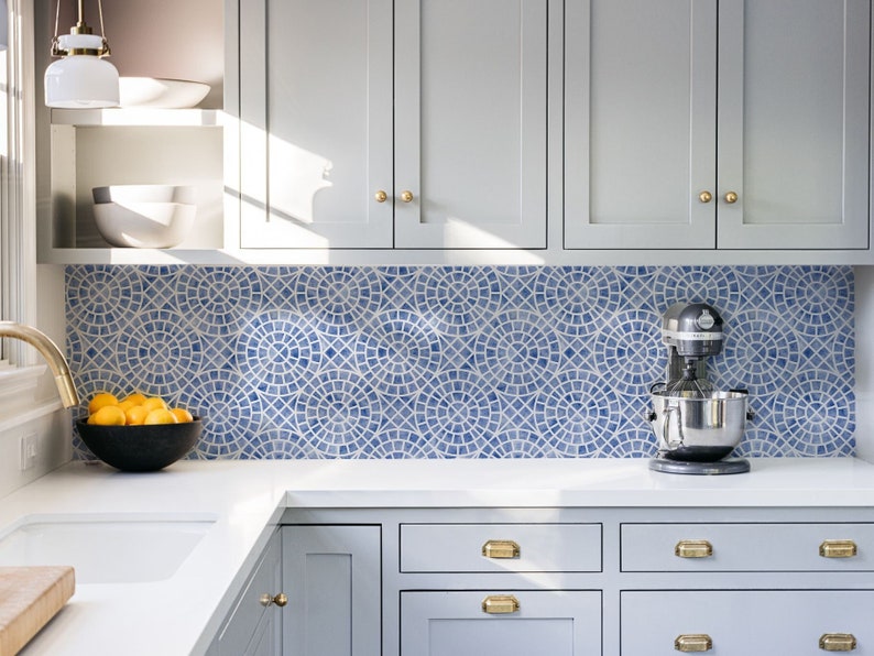May include: A white kitchen with gray cabinets and a blue and white patterned tile backsplash. A stand mixer is on the counter in front of the backsplash.