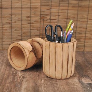 May include: Two wooden desk organizers. One is cylindrical with vertical grooves and holds scissors, pens, and pencils. The other is a similar design, but lying on its side. Both are made of light brown wood.
