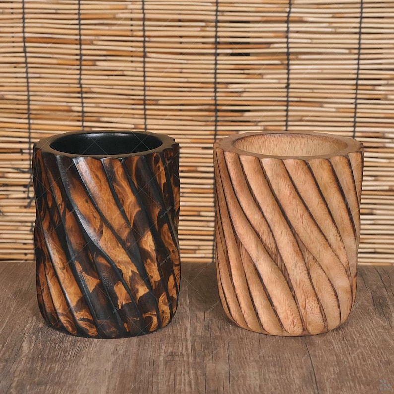 May include: Two wooden cylindrical containers with a carved, spiral design. One is dark brown with black accents, and the other is light brown. The containers sit on a wooden surface against a bamboo blind background.