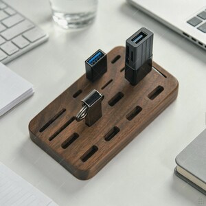 May include: A rectangular dark brown wooden organiser stand featuring multiple horizontal slots for storage. Three black USB flash drives and card readers are inserted into the slots on the top surface of the wooden base, which has a smooth, polished finish.