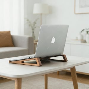 May include: A silver laptop sits on a wooden laptop stand. The stand is made of light brown wood with a triangular design. The laptop is open, displaying a white Apple logo. The stand is on a white table.