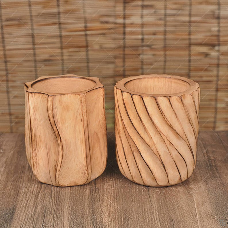 May include: Two wooden cylindrical containers with unique carved designs. One has a geometric, faceted shape, while the other features a spiral groove pattern. Both are made of light-colored wood and sit on a wooden surface, suggesting a natural, rustic aesthetic.