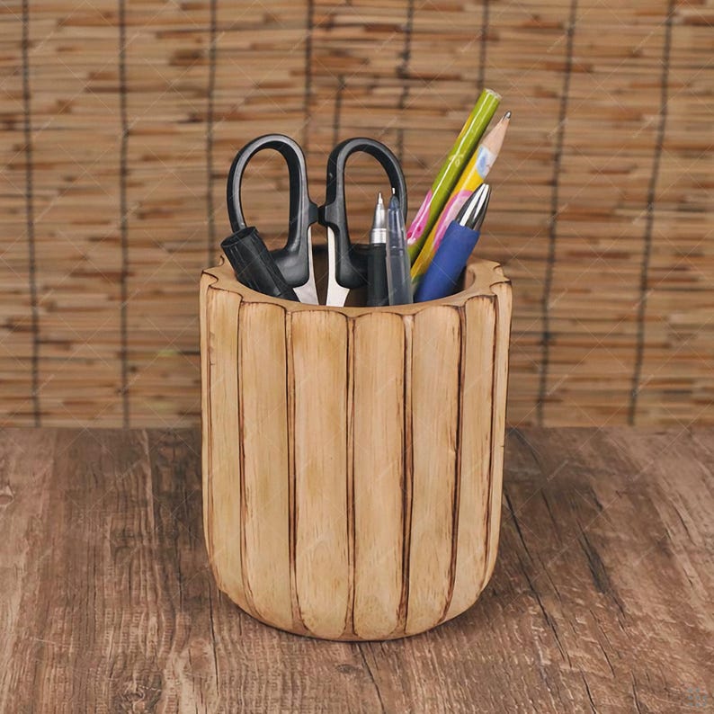 May include: A light brown wooden desk organizer with vertical grooves, holding black scissors, pens, and pencils. The organizer sits on a wooden surface, with a bamboo blind in the background.