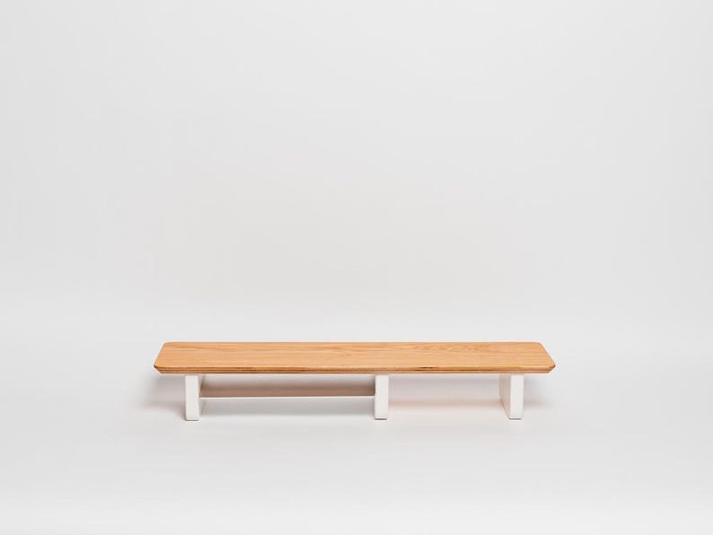 May include: A rectangular wooden shelf featuring a natural light brown wood grain top surface with rounded corners. The shelf is supported by three vertical white legs positioned along the underside, providing a stable base for the horizontal platform.