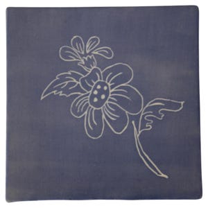 Puede incluir: Azulejo decorativo cuadrado azul marino con un diseño floral blanco. El diseño incluye una flor grande con un centro detallado y una flor más pequeña encima, conectadas por un tallo y hojas. El azulejo tiene un acabado mate.