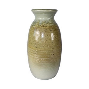 Może przedstawiać: Ręcznie wykonany ceramiczny wazon o nakrapianej, teksturowanej powierzchni. Wazon ma gradient kolorów, przechodzący od kremowobiałej podstawy do odcieni beżu i oliwkowej zieleni u góry. Ma zaokrąglony korpus i wąską szyjkę.