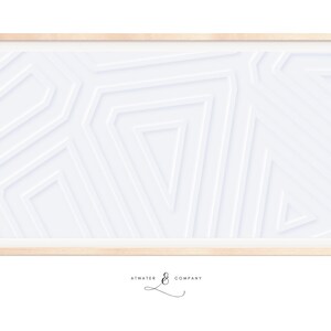 Op de afbeelding: Een ingelijste abstracte kunstprint met een wit geometrisch ontwerp op een witte achtergrond. De lijst is gemaakt van licht hout.