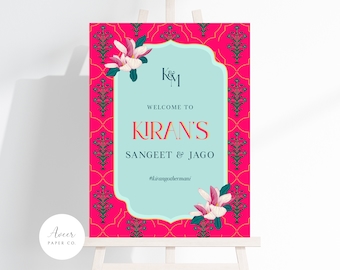 May include: A welcome sign for a Sangeet & Jago event with a pink and blue floral design. The sign says "Welcome to Kiran's Sangeet & Jago #kiransothermani".