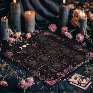 May include: A black tarot reading cloth featuring a numbered grid from one to ten, decorated with pink roses, celestial motifs, and a moon phase icon. The cloth is surrounded by several lit gray and orange pillar candles and scattered pink flower petals.
