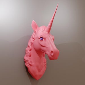 May include: A pink unicorn head wall decoration featuring a spiralled horn and detailed mane. The sculpture has purple eyes and is mounted on a neutral-coloured wall. The unicorn is a mythical creature.