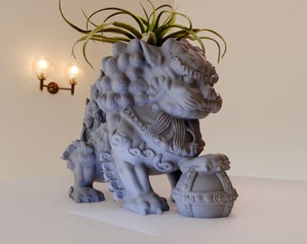 May include: A gray stone lion statue with intricate details, holding a round orb in its paw. The statue is a planter and has a small green plant growing out of its head.