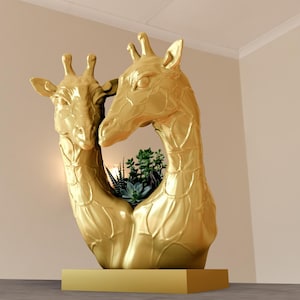 May include: A golden giraffe sculpture with two giraffe heads facing each other, forming a heart-shaped opening. The opening is filled with green plants. The sculpture is on a gold rectangular base.