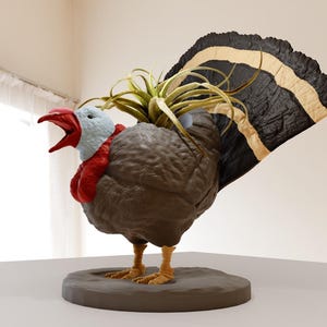 May include: A brown and gray turkey figurine with a white and black tail. The turkey has a red wattle and a blue head. A green plant is growing out of the turkey's back.