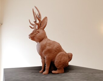 May include: A brown ceramic sculpture of a rabbit with antlers. The rabbit is sitting on a dark surface.