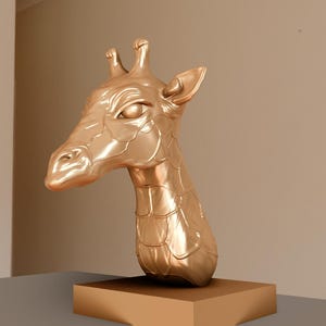 May include: A gold-colored giraffe head sculpture on a wooden base. The sculpture is detailed with textured skin and a realistic expression.