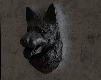 Puede incluir: Una escultura de cabeza de perro pastor alemán negro montada en una pared gris. La escultura es realista y detallada, con un pelaje texturizado y una boca ligeramente abierta.