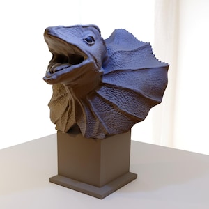 Peut inclure: Une sculpture en 3D imprimée en gris d'un lézard à collerette avec la bouche ouverte, sur un piédestal brun.