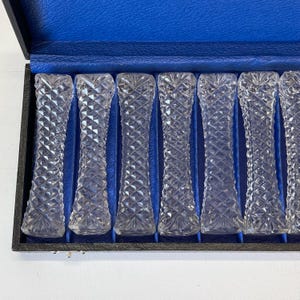 May include: A set of ten clear glass knife rests in a black velvet lined box. The knife rests are in a diamond pattern.