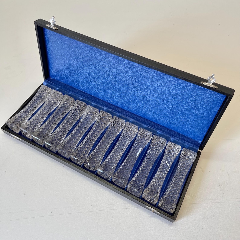 May include: A set of 12 clear glass chopsticks in a black box with a blue velvet lining.