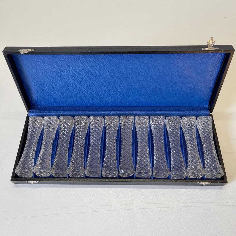 May include: A set of 16 clear glass butter knives in a black box with a blue velvet lining. The knives have a diamond pattern.