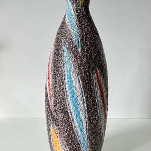 Op de afbeelding: Een hoge, bruine vaas met textuur, een smalle hals en een brede basis. De vaas heeft kleurrijke diagonale strepen in geel, rood, blauw en wit. De vaas is ongeveer 30 cm hoog.