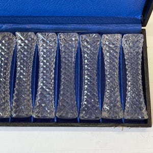 May include: Set of eight clear glass crystal chopsticks in a black velvet lined box. The chopsticks are in a row and have a diamond pattern.
